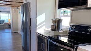 A modern kitchen with stainless steel appliances, white cabinetry, and a wooden ceiling. - Waterfront Beach House (Clinton)