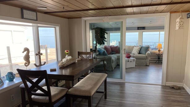 A cozy dining area with a wooden table, cushioned chairs, and a view of the beach. - Waterfront Beach House (Clinton)