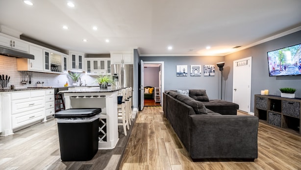 A modern kitchen with white cabinetry, a central island, and a black trash bin. - Mega House: 7 bed 3 bath! King & Queen beds! (Irving)