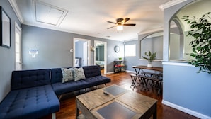 A living room with a dark blue sectional sofa, a wooden coffee table, and a ceiling fan. - Mega House: 7 bed 3 bath! King & Queen beds! (Irving)