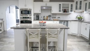 A modern kitchen with white cabinets, granite countertops, stainless steel appliances, and a central island with bar stools. - Mega House: 7 bed 3 bath! King & Queen beds! (Irving)