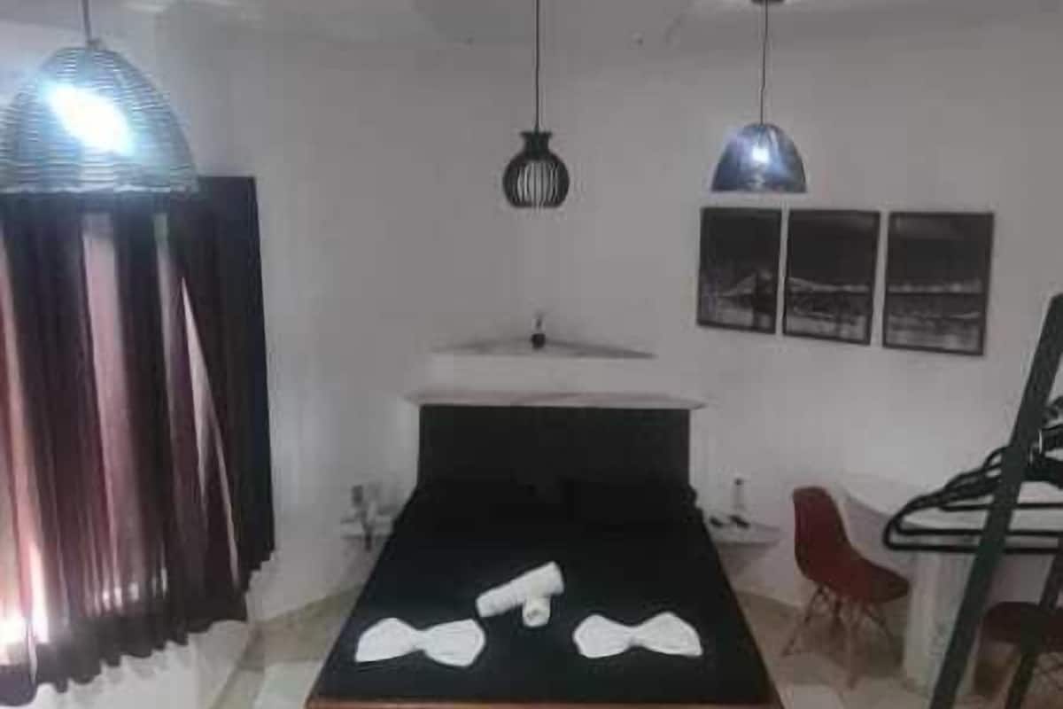 A bedroom with a bed, a desk, a chair, a window, and a ceiling fan.