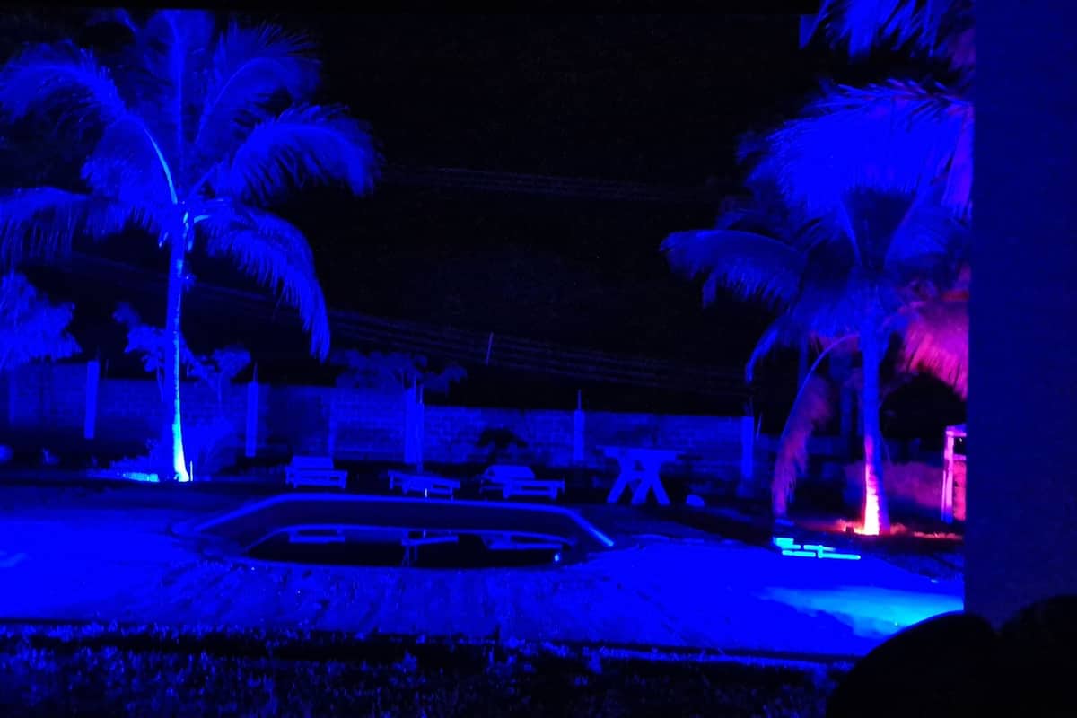 A nighttime view of a resort area with palm trees and a pool.