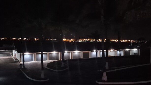 Vista nocturna de un estacionamiento con hileras de edificios iluminados al fondo.