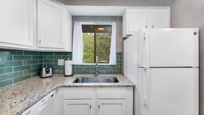 A compact kitchen with white cabinets, a granite countertop, a built-in dishwasher, and a window with a view of greenery. - Pinseeker, a greenside condo on No. 5 - Walk to Pinehurst Clubhouse (Pinehurst)