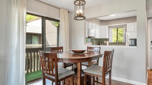A dining area with a round wooden table and four chairs, a bowl on the table, and a kitchen in the background. - Pinseeker, a greenside condo on No. 5 - Walk to Pinehurst Clubhouse (Pinehurst)