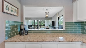 Enjoy meals in this kitchen with a granite countertop and white cabinetry, featuring a coffee maker and a dining area with outdoor views.