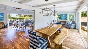 Amplia sala de estar con una mesa de comedor de madera, sillas a rayas y un banco. Hay dos lámparas colgantes y un ventanal con vista a la vegetación.