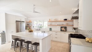 Una cocina moderna con armarios blancos, una isla grande con taburetes, un refrigerador y una estufa a gas.