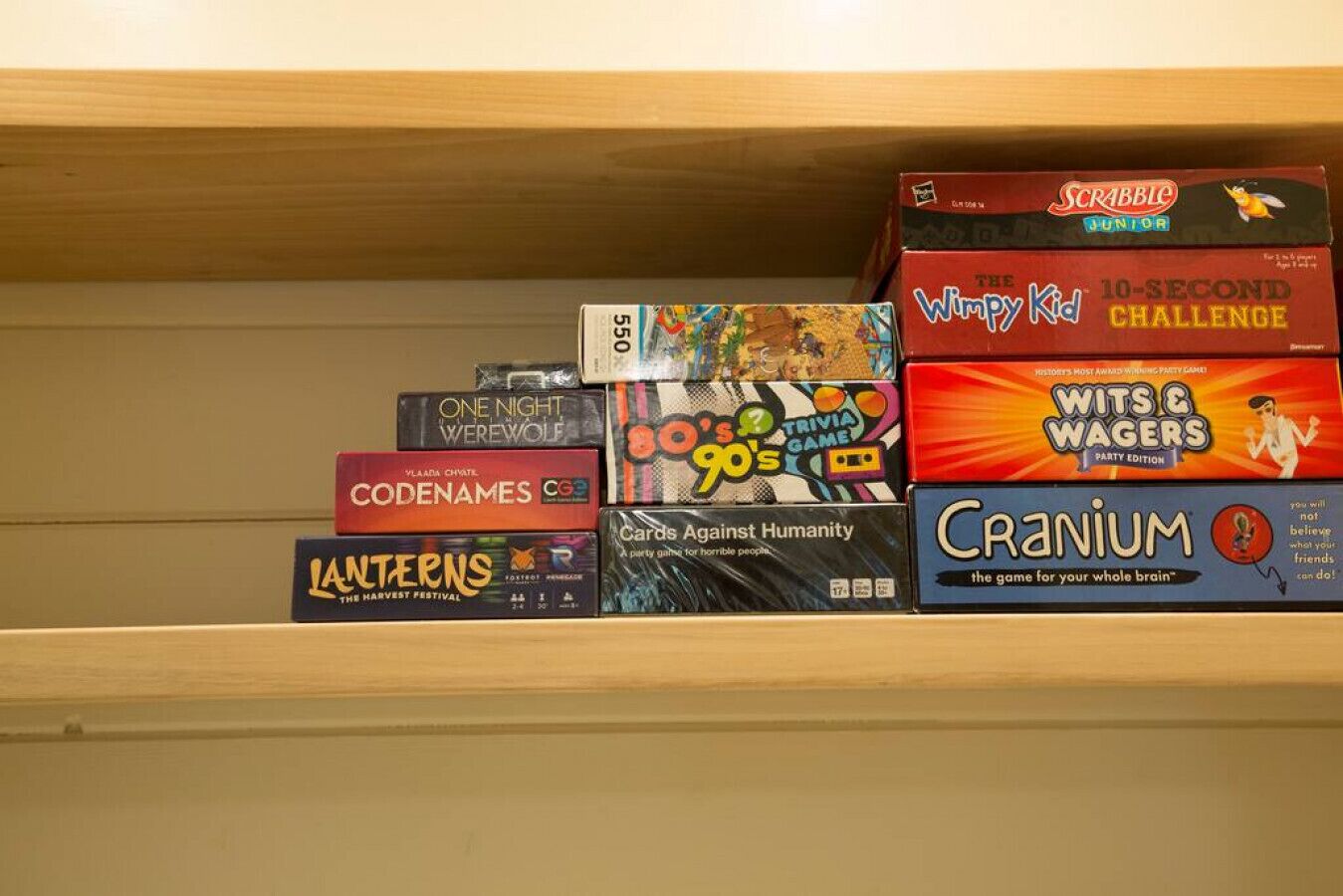 A shelf with various board games including Scrabble Junior, Wits & Wagers, Trivia Game, and others.