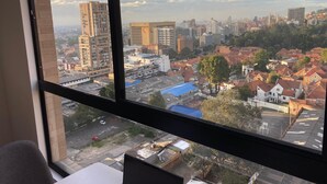 Paesaggio urbano visibile da una finestra, con edifici residenziali e commerciali, cielo sereno e strada trafficata.