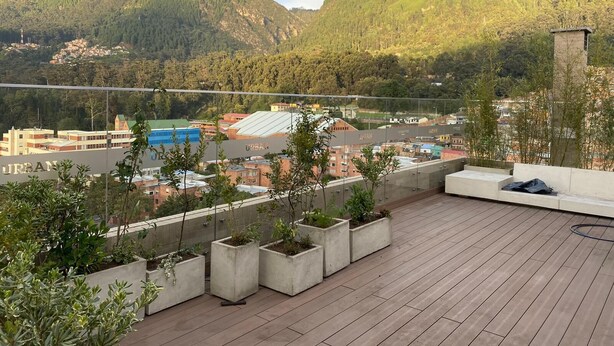 Una terrazza sul tetto con fioriere in cemento, vista sulla città e montagne sullo sfondo.