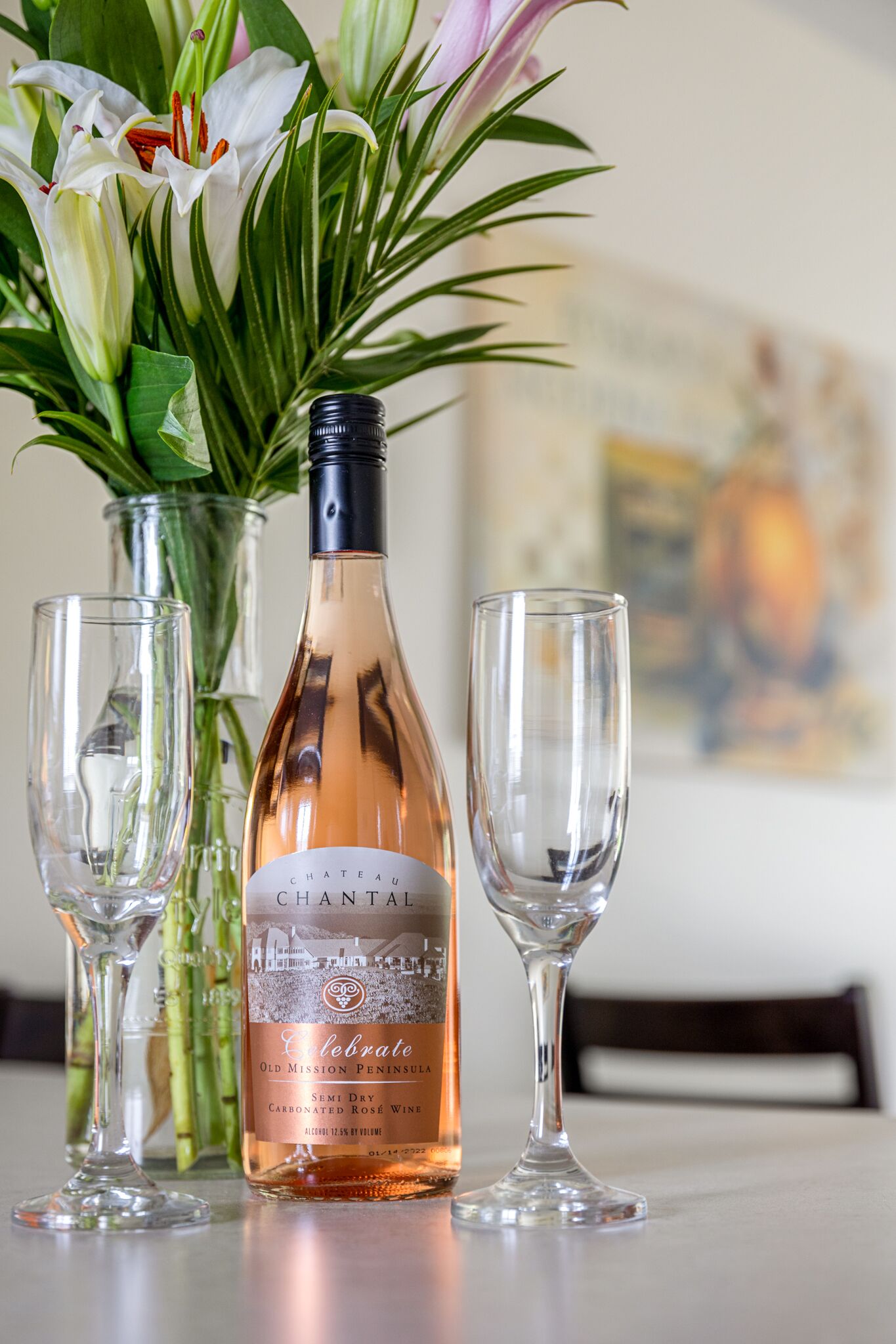 Una botella de vino Chateau Chantal, dos copas de vino vacías y un jarrón con flores sobre una mesa.