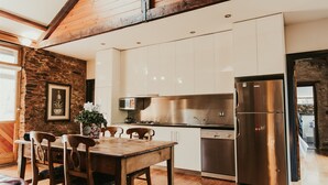 A modern kitchen with white cabinets, a stainless steel refrigerator, and a wooden dining table with chairs. - Mintaro Cottage (Mintaro)