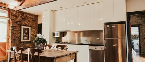 A modern kitchen with white cabinets, a stainless steel refrigerator, and a wooden dining table with chairs.
