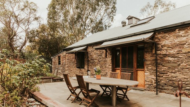A stone house with a patio, wooden furniture, and a potted plant. - Mintaro Cottage (Mintaro)