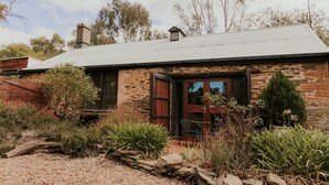 A stone house with a metal roof, a wooden door, and a small porch with a chair. - Mintaro Cottage (Mintaro)