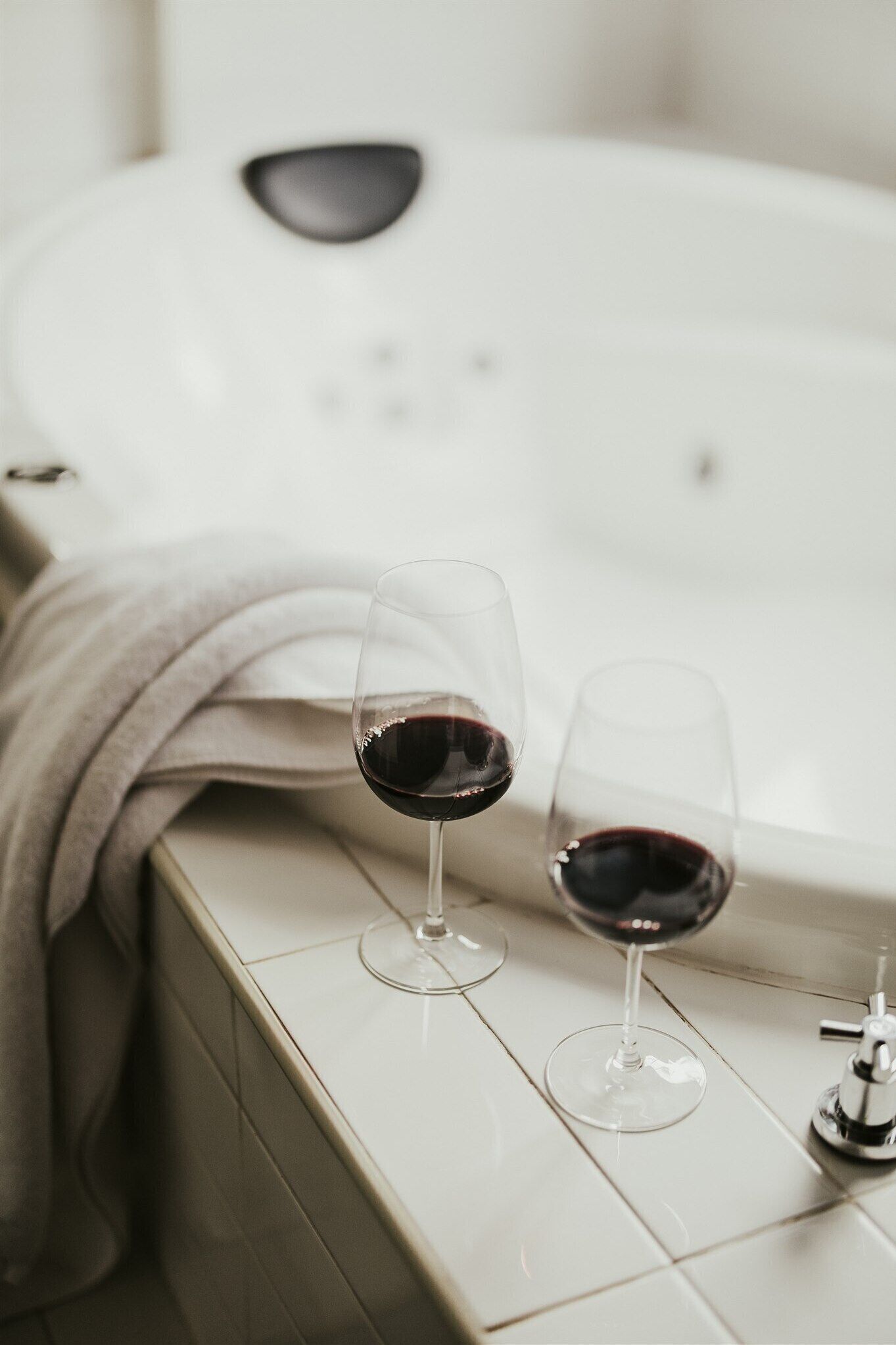 Dos copas de vino sobre una encimera de baño, con una bañera al fondo.
