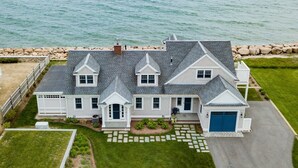 A large, two-story house with a garage, a well-maintained lawn, and a view of the ocean.