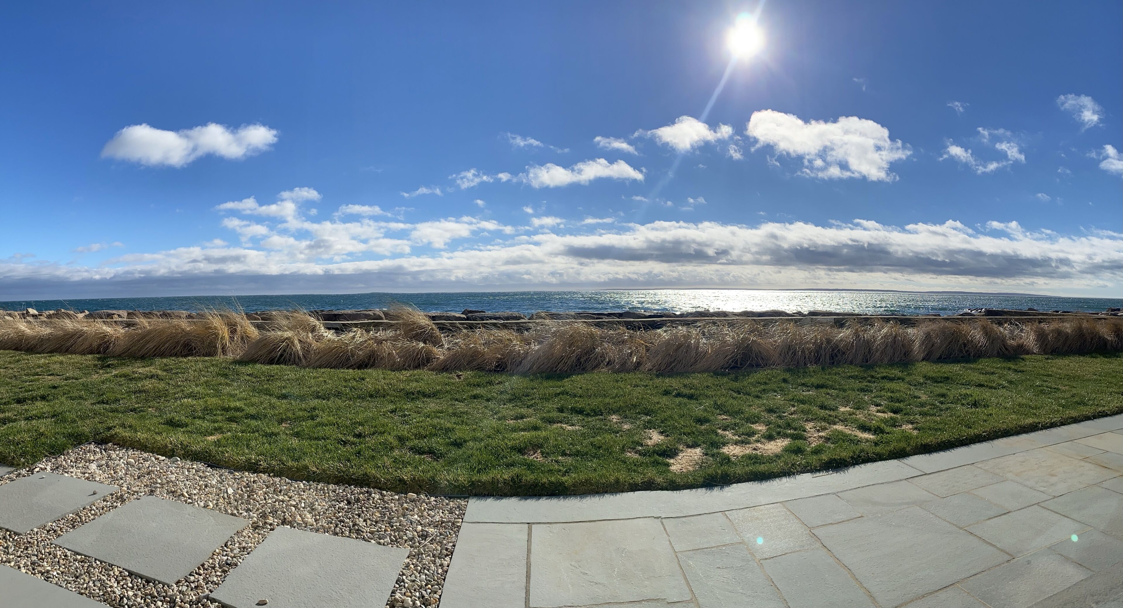 Eine Küstenlandschaft mit blauem Himmel, einem gepflasterten Weg und einer Rasenfläche mit Blick aufs Meer.