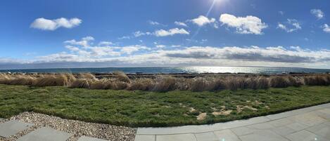 Eine Küstenlandschaft mit blauem Himmel, einem gepflasterten Weg und einer Rasenfläche mit Blick aufs Meer.