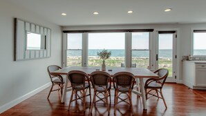 A dining area with a view of the ocean, featuring a wooden table and wicker chairs.