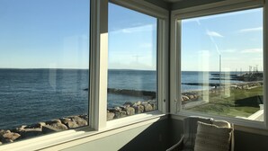 A room with a view of the sea through large windows, a chair, and a view of the coastline.