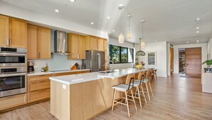 A modern kitchen with wooden cabinets, stainless steel appliances, and a central island with bar stools. - Maui Resort Rentals: Luana Garden Villas 15B – Modern 3BR Villa at Kaanapali’s Newest Luxury Residences! (Lahaina)