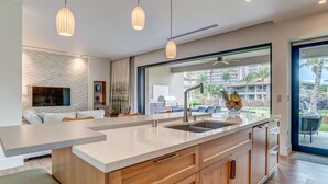 A modern kitchen with a large island, wooden cabinets, and a view of a pool and palm trees.