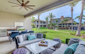 Uma área externa moderna para relaxamento, com sofá, mesa de jantar e churrasqueira, com vista para um jardim bem cuidado e edifícios do hotel.