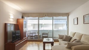 A living room with a flat-screen TV, wooden furniture, a sofa, and a balcony with a view of buildings. - EXCELLENT APARTMENT NEXT BEACH 7 (Tossa de Mar)