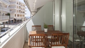 A balcony with a wooden table and chairs, a potted plant, and a view of the street and buildings. - EXCELLENT APARTMENT NEXT BEACH 7 (Tossa de Mar)
