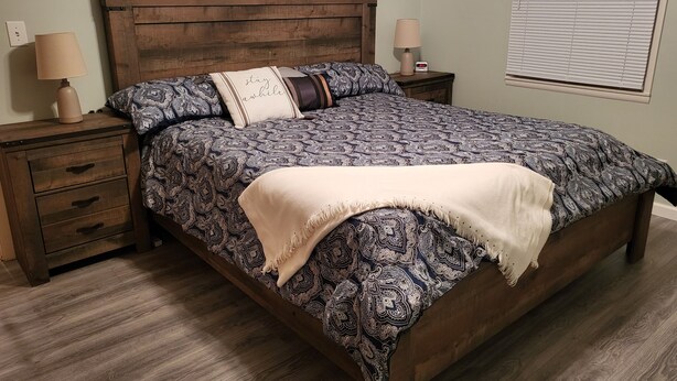 Une chambre à coucher avec un lit en bois, une literie à motifs, une table de chevet avec une lampe et une petite table de nuit avec une horloge.