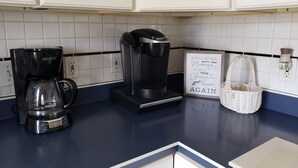 Une cuisine équipée d’une machine à café, d’une bouilloire et d’une affiche accrochée au mur.