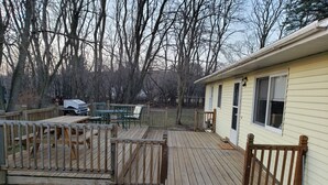 Une terrasse en bois avec des tables et des chaises pour pique-niquer, une petite maison avec une fenêtre et une clôture en bois.