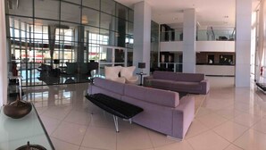 A spacious lobby with a modern design, featuring a seating area with sofas and a bench, a glass wall providing a view of the outside, and a reception desk. - Studio Business West Flat (Mossoró)