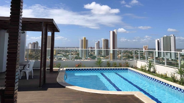 A rooftop pool with a cityscape view, surrounded by a wooden deck and a pergola. - Studio Business West Flat (Mossoró)