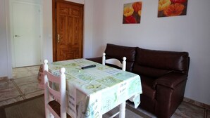 A room with a dining table, a brown leather sofa, a wooden door, and two paintings on the wall. - Apartment in Conil de la Frontera, Cádiz (Conil de la Frontera)
