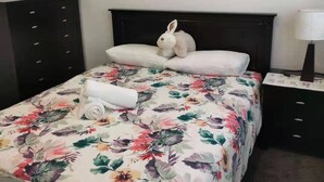Ein Bett mit blumigem Überwurf, einem zusammengerollten Handtuch und einem Stoff-Hasen.