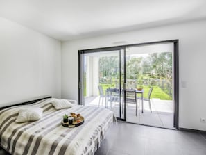 Un dormitorio con cama, una bandeja de alimentos para el desayuno y un ventanal corredero que da a un patio exterior con mesa y sillas.