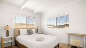 A modern bedroom with a wooden bed, two bedside tables with lamps, a small desk, and a fluffy chair. - NEW! Ocean View Beach House Steps from the Sand  (Manhattan Beach)