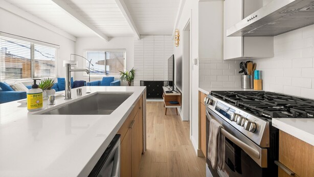 A modern kitchen with white cabinetry, a stainless steel stove, and a large island with a sink. - NEW! Ocean View Beach House Steps from the Sand  (Manhattan Beach)