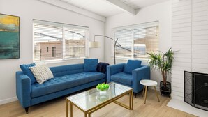 A modern living room with a blue sofa, a glass coffee table, and a fireplace. - NEW! Ocean View Beach House Steps from the Sand  (Manhattan Beach)