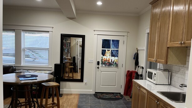 A modern kitchen with wooden cabinets, a marble countertop, a built-in microwave, and a dining area with a round table and stools. - Country Blue is close to forest trails and beach (Qualicum Beach)