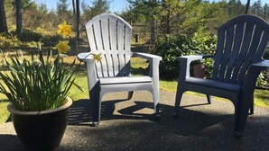 Two Adirondack chairs in a garden setting with a potted plant and yellow flowers. - Country Blue is close to forest trails and beach (Qualicum Beach)