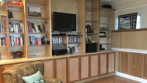 A living room with wooden cabinets, a bookshelf, a flat-screen TV, and a patterned armchair. - Country Blue is close to forest trails and beach (Qualicum Beach)