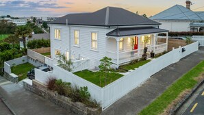 A two-story white house with a dark roof, a front porch, and a fenced yard.