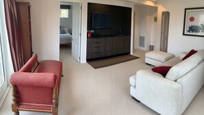 A modern living room with a red armchair, a white sofa, and a kitchen area with a flat-screen TV.