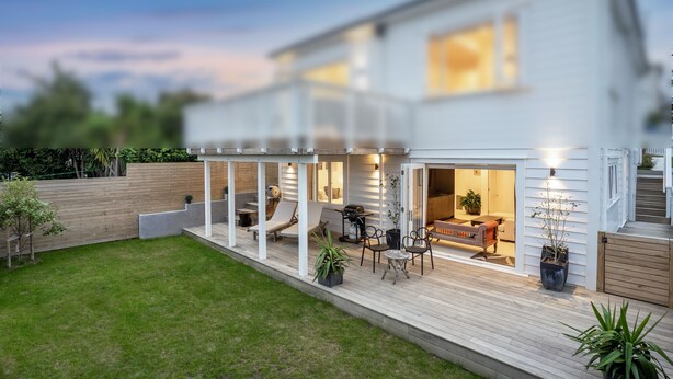 A modern two-story house with a covered patio area, outdoor seating, and a well-maintained lawn.