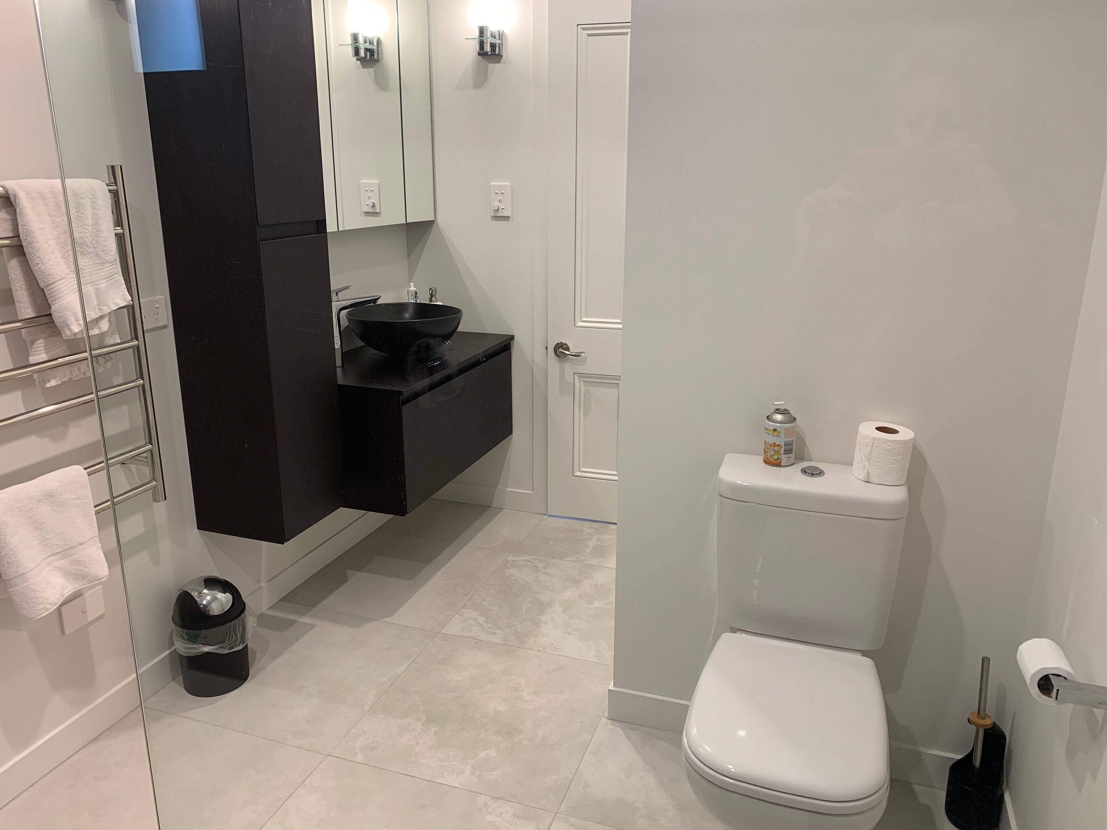 A modern bathroom with a black vanity, white toilet, and a glass shower enclosure.